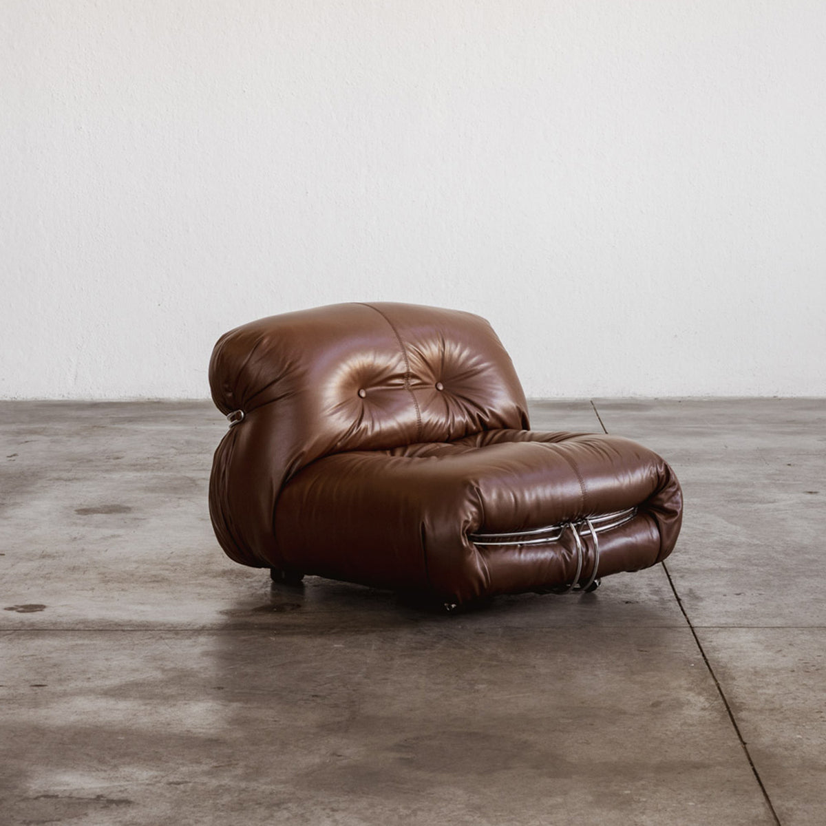 Brown leather armchair on a wooden floor with a white wall background