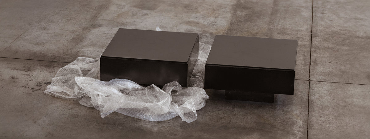 Two dark rectangular objects on a concrete floor with plastic wrap.