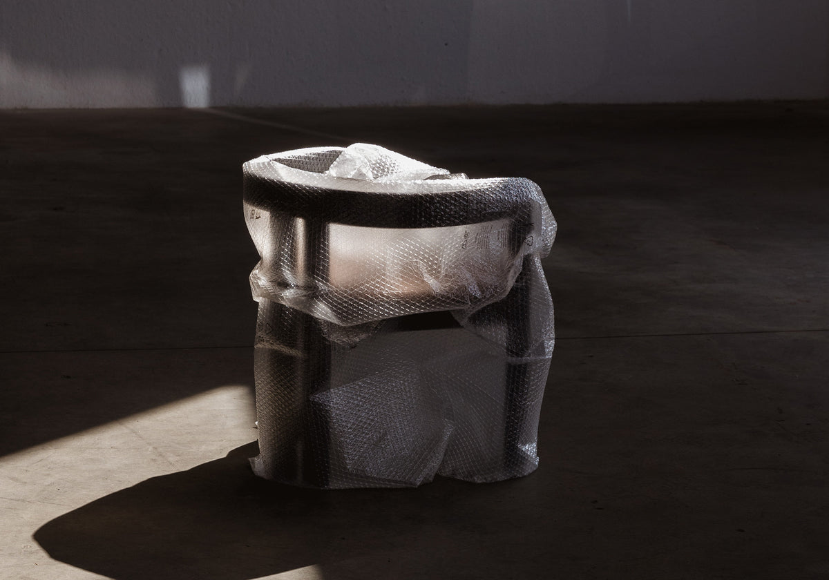 Pigreco chair wrapped in plastic on a dark surface