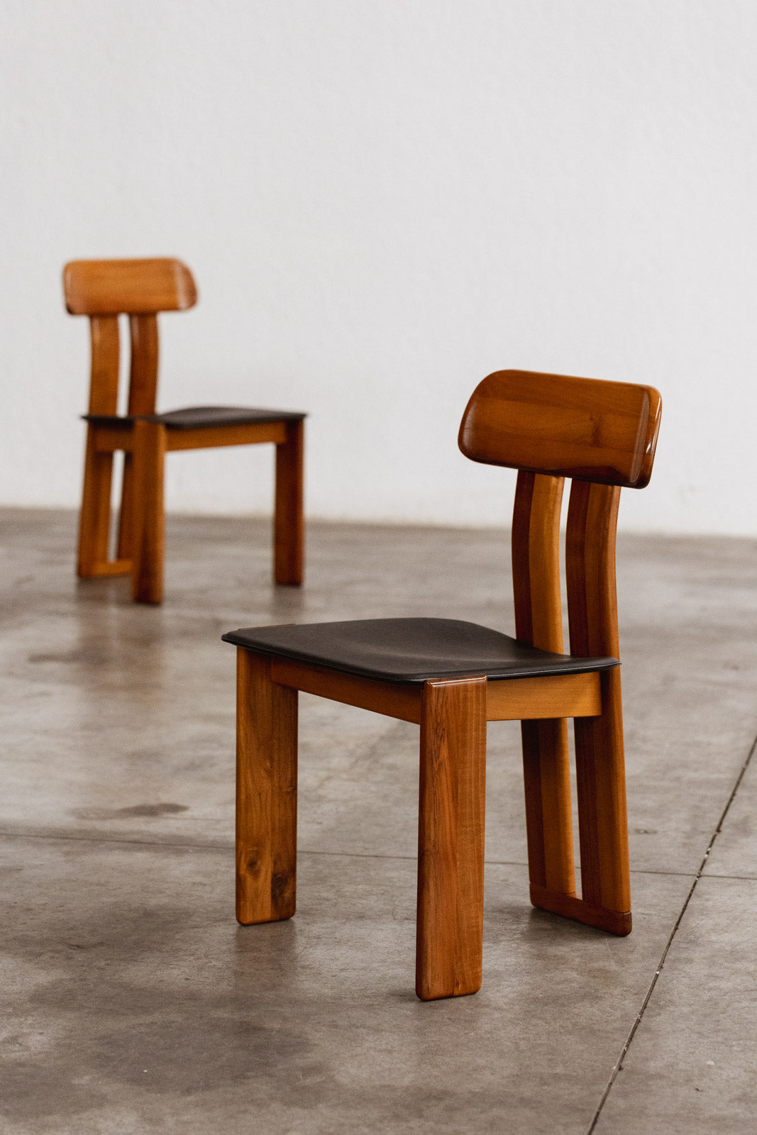 Two wooden chairs with black seats on a concrete floor.