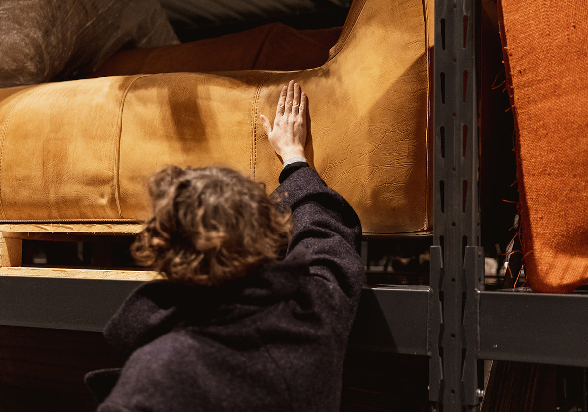 Person touching a brown leather couch in Modernab warehouse