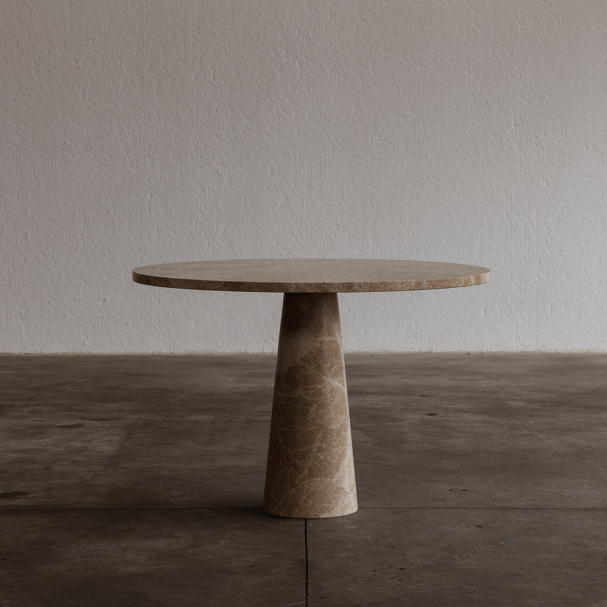 Round stone table with a cylindrical base on a wooden floor against a plain wall.